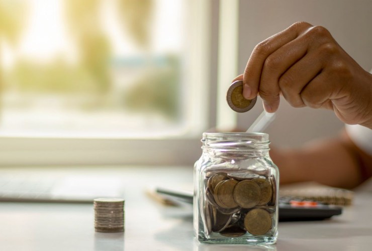 Persona che mette una moneta in un contenitore di vetro