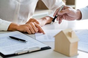 Persone che firmano un contratto di affitto e miniatura di una casa