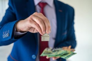 Persona che ha in mano banconote e la miniatura di una casa
