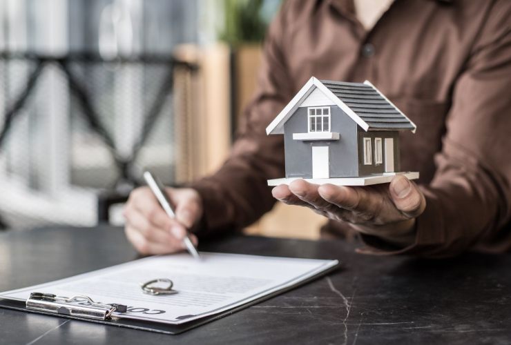 Persona che firma un contratto mentre in mano ha la miniatura di una casa