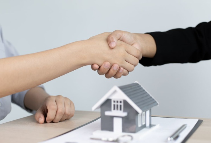 Persone che si stringono la mano dopo aver firmato un contratto di affitto e miniatura di una casa