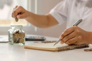 Persona che fa dei calcoli e mette una moneta in un vasetto di vetro